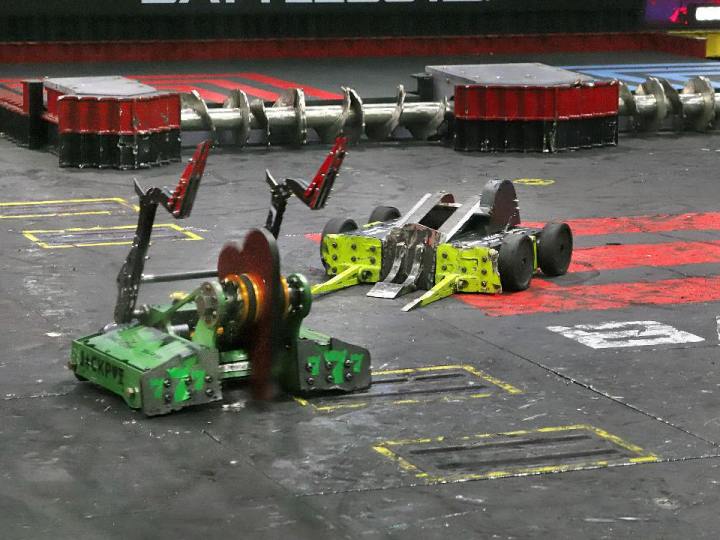 Battlebots Whiplash fighting with another robot. Green robot with metal arms up with Whiplash yellow robot preparing for attack in Battlebots arena